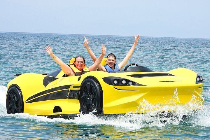 A couple of people in a yellow car on the water.